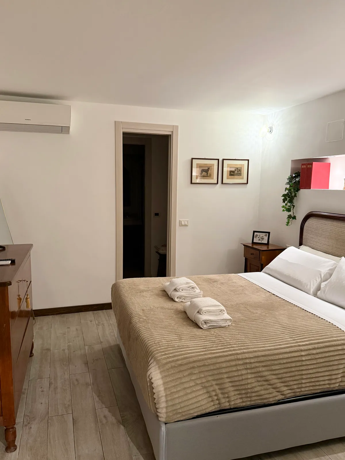 La camera vista verso la porta, con i quadretti e il condizionatore
