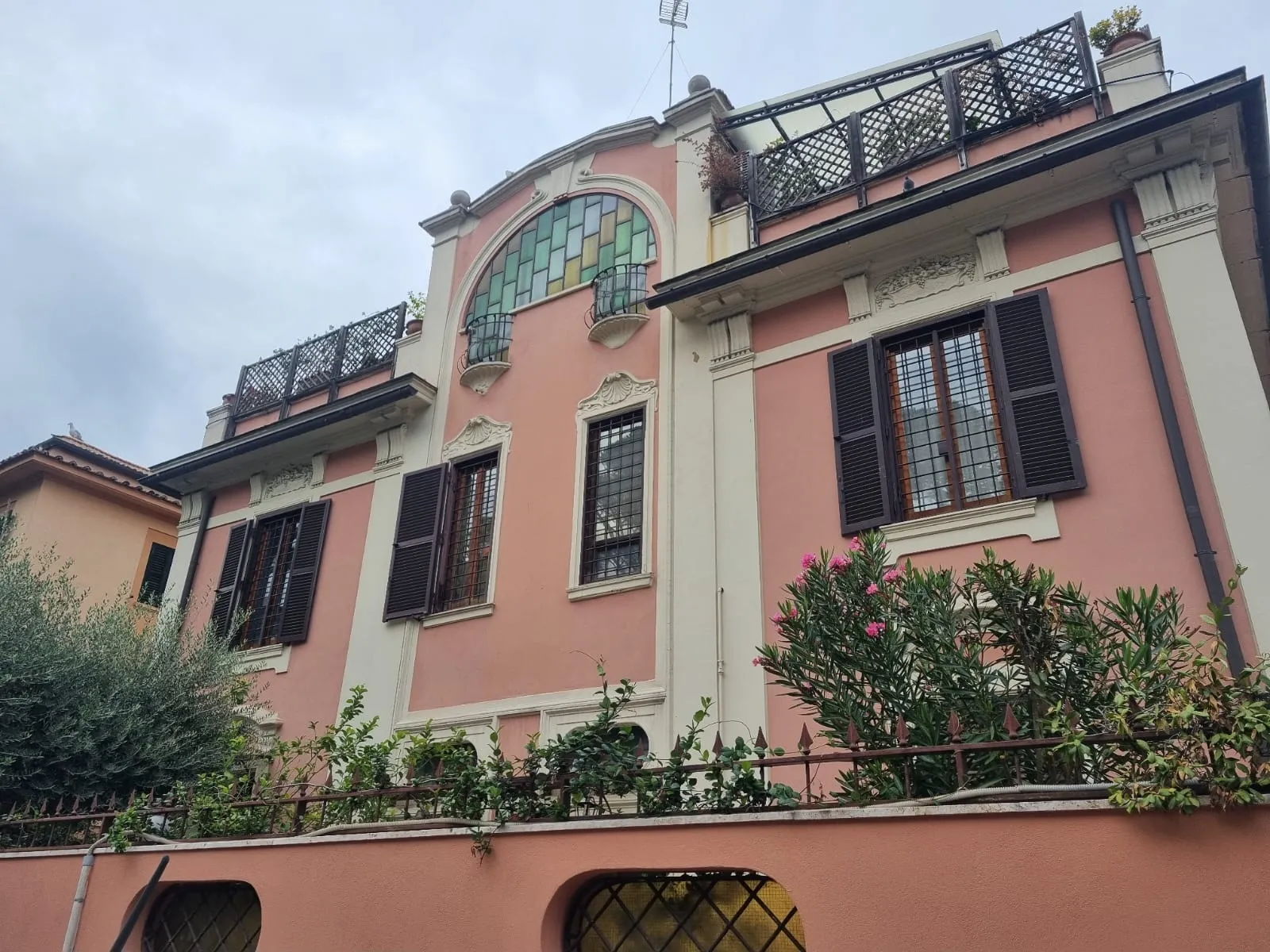 La facciata rosa del villino del 1913 con la vetrata ad arco, tra gli oleandri